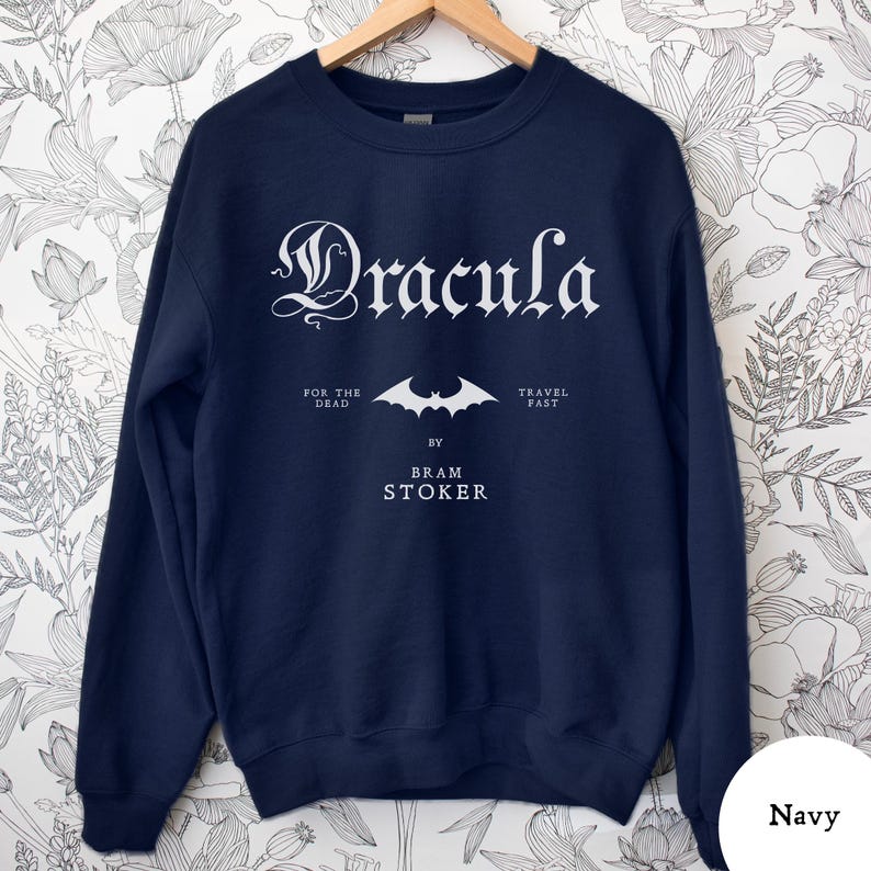 Op de afbeelding: Marineblauwe sweatshirt met het woord "Dracula" in een gotisch lettertype. Daaronder een vleermuisafbeelding en de tekst "For the Dead", "Travel Fast" en "By Bram Stoker".