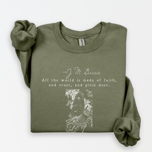 May include: Olive green sweatshirt with the quote "All the world is made of faith, and trust, and pixie dust" by J.M. Barrie. A white butterfly illustration is below the quote. The sweatshirt has a crew neck and long sleeves.