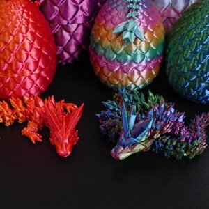 Pu&ograve; includere: Una collezione di uova di drago e draghi articolati stampati in 3D. Le uova, con un motivo a scaglie, sono nei toni del rosso, viola, verde e blu. Sono visibili anche due draghi, uno arancione e uno multicolore.