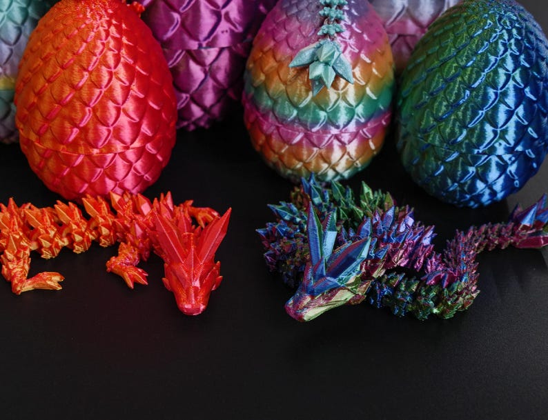 Pu&ograve; includere: Una collezione di uova di drago e draghi articolati stampati in 3D. Le uova, con un motivo a scaglie, sono nei toni del rosso, viola, verde e blu. Sono visibili anche due draghi, uno arancione e uno multicolore.