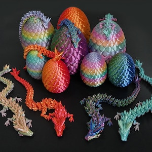 以下が含まれることがあります： 虹色のドラゴンエッグのオーナメントが7つあり、それぞれに独特の色と模様が施されています。卵は、いくつかが重なり合って、塊状に配置されています。また、ピンク、ブルー、グリーン、レッドなど、さまざまな色の折り紙のドラゴンが5匹います。