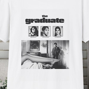 May include: A white short-sleeved t-shirt featuring a black and white graphic print from the film The Graduate. The design includes the movie title, three small portrait photos, and a larger scene showing a person standing in a room.