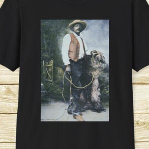 May include: Black t-shirt featuring a vintage-style image of a man in a hat and vest, holding a rope and standing with a large dog. The image has a sepia tone, giving it a classic, old-fashioned look. The shirt is a classic crew neck.