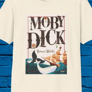 May include: Cream-colored t-shirt featuring the title "Moby Dick" in a vintage font, with a nautical wheel graphic. The design includes illustrations of a whale, sailing ships, and the author's name, Herman Melville.