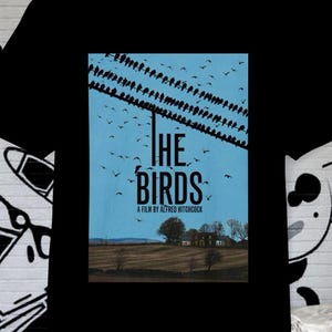 May include: Black t-shirt featuring a movie poster design for "The Birds" by Alfred Hitchcock. The poster shows birds on a wire against a blue sky, with the film title prominently displayed. The shirt is a classic crew neck.