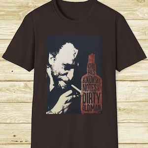 以下が含まれることがあります： 男性の白黒ポートレートが描かれた、濃い茶色のTシャツ。画像には、赤いボトル型のデザインで「Charles Bukowski Notes of a Dirty Old Man」というテキストが含まれています。