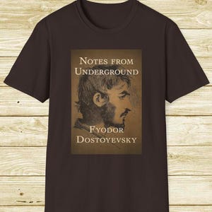May include: A dark brown t-shirt featuring a sepia-toned graphic from Fyodor Dostoevsky's "Notes from Underground." The graphic includes a portrait and the book title.