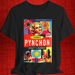 May include: Black t-shirt featuring a colorful graphic design from the novel "Gravity's Rainbow" by Thomas Pynchon. The design includes a portrait of a woman, a star, and a rocket ship. The text "Pynchon" is prominently displayed.