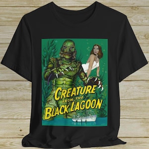 Könnte beinhalten: Schwarzes T-Shirt mit einem Vintage-Filmplakat-Design. Die Grafik zeigt die Kreatur aus der schwarzen Lagune, ein grünes Monster, mit einer Frau und dem Text "Creature from the Black Lagoon".