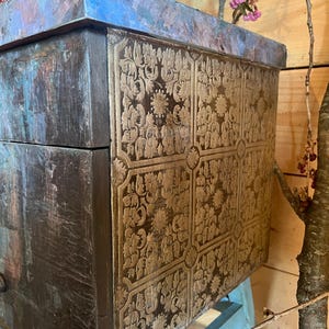 May include: A wooden box with a distressed blue and brown finish. The box has a gold patterned design on the front and a blue top.