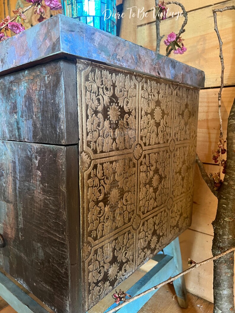 May include: A wooden box with a distressed blue and brown finish. The box has a gold patterned design on the front and a blue top.