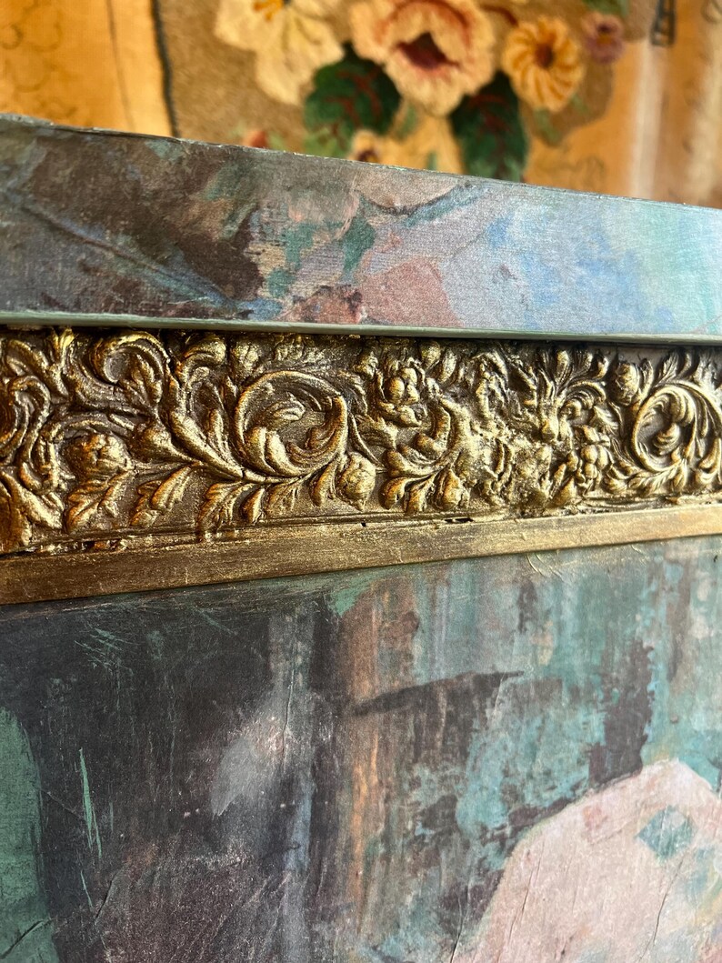 May include: A close-up of a dark green and blue painted wooden frame with a gold ornate border. The frame is textured and has a distressed look.