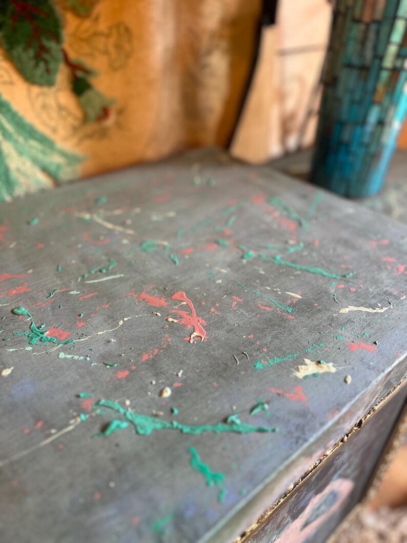 May include: A gray wooden box with a distressed finish. The box is decorated with splashes of green, pink, and white paint.