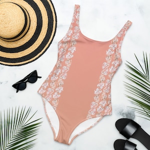 May include: A peach-colored swimsuit with a white floral pattern on the sides. The swimsuit has a scoop neck and thin straps.
