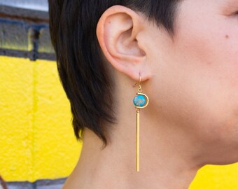 Peut inclure: Boucles d'oreilles pendantes dorées avec une pierre turquoise et une longue barre dorée fine.