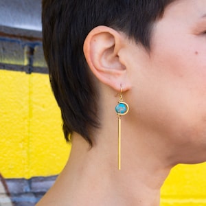 May include: Gold dangle earrings with a turquoise stone and a long, thin gold bar.