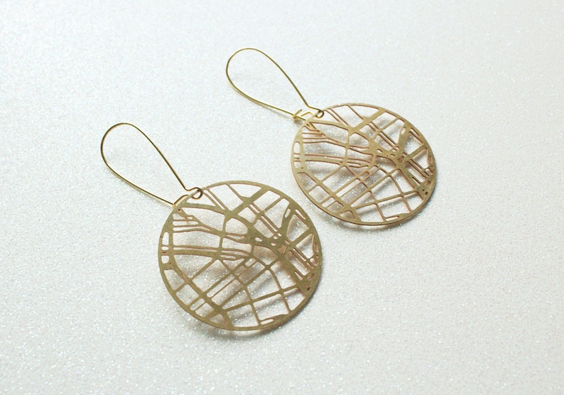 May include: A pair of gold-toned earrings featuring a circular design with a detailed city map pattern.