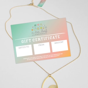 May include: A gold gift certificate with a teal and pink gradient background. The certificate is for a tea leaf jewelry store. The text on the certificate reads "a tea leaf 000.JEWELRY0000 GIFT CERTIFICATE GIFTED TO FROM AMOUNT Redeemable only at the online store "A Tea Leaf" on www.atesicof.etsy.com this gift certificate expires after one year from date of payment."