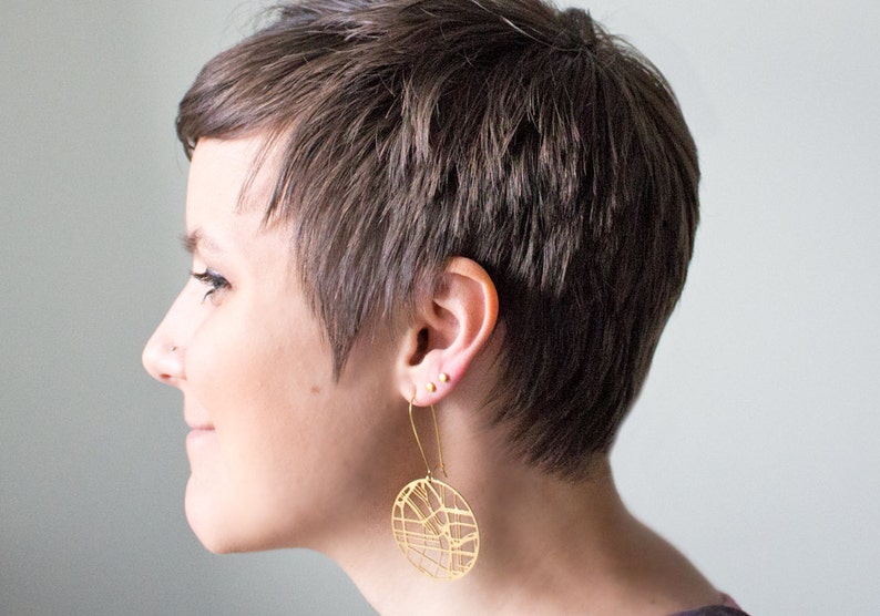 May include: A person with short brown hair wearing a gold geometric earring. The earring is a circle with a detailed design.