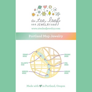 May include: A teal and gold illustration of a map of Portland, Oregon with the text "a tea leaf JEWELRY" and "www.atealeafjewelry.com". The map shows the Willamette River and several bridges, including the Fremont Bridge, Broadway Bridge, Steel Bridge, Morrison Bridge, and Burnside Bridge. The text "Portland Map Jewelry" and "Made with &hearts; in Portland, Oregon" are also included.
