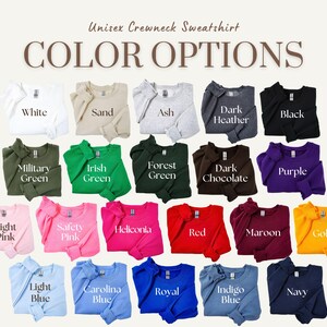 Op de afbeelding: Een kleurenkaart met 18 verschillende kleuropties voor een unisex crewneck sweatshirt. De kleuren omvatten wit, zand, as, donkergrijs melange, zwart, legergroen, Iers groen, bosgroen, donker chocolade, paars, lichtroze, veiligheidsroze, heliconia, rood, bordeauxrood, goud, lichtblauw, Carolina blauw, koninklijkblauw, indigo blauw en marineblauw.