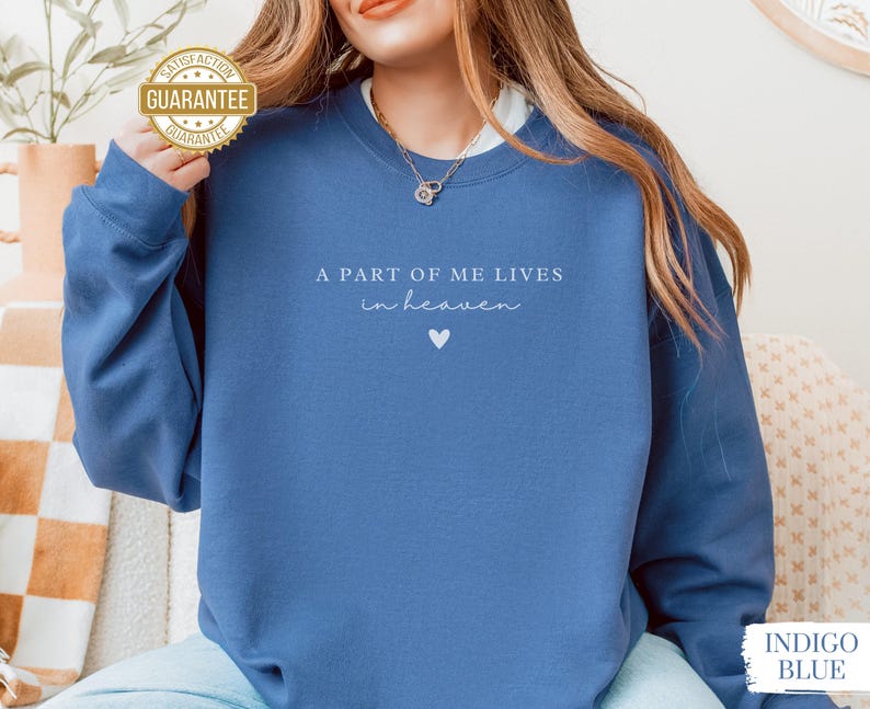 Op de afbeelding: Een blauw sweatshirt met de tekst "A part of me lives in heaven" en een kleine hartvormige afbeelding.