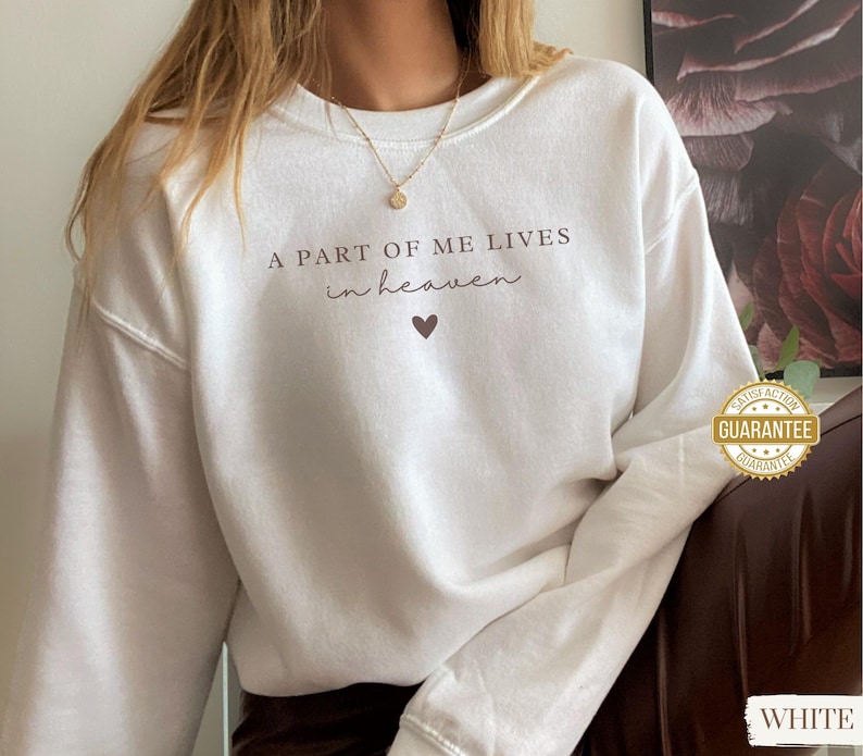 Op de afbeelding: Witte trui met de tekst "A part of me lives in heaven" en een klein hartje.