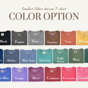 K&ouml;nnte beinhalten: Eine Auswahl an Comfort Colors Unisex-T-Shirts in verschiedenen Farben, darunter Schwarz, Grau und Blau. Das Bild zeigt die verf&uuml;gbaren Farboptionen mit Namen wie "Senf", "Seafoam" und "Berry" unter jedem Shirt.