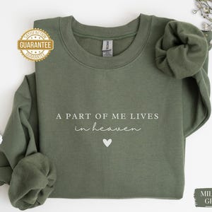 Op de afbeelding: Een groen sweatshirt met de tekst "Een deel van mij leeft in de hemel" en een kleine hartvormige afbeelding. Het sweatshirt is gemaakt van een zacht, comfortabel materiaal.