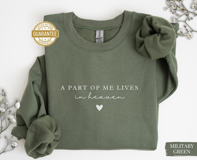 Op de afbeelding: Een groen sweatshirt met de tekst "Een deel van mij leeft in de hemel" en een kleine hartvormige afbeelding. Het sweatshirt is gemaakt van een zacht, comfortabel materiaal.