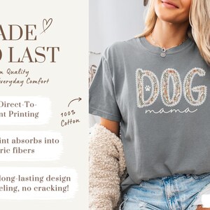K&ouml;nnte beinhalten: Ein graues T-Shirt mit den Worten "DOG mama" in einem floralen Design. Das Shirt besteht aus 100 % Baumwolle und verf&uuml;gt &uuml;ber einen Direktdruck f&uuml;r ein weiches, langlebiges Design. Der Text "MADE TO LAST" ist ebenfalls sichtbar.