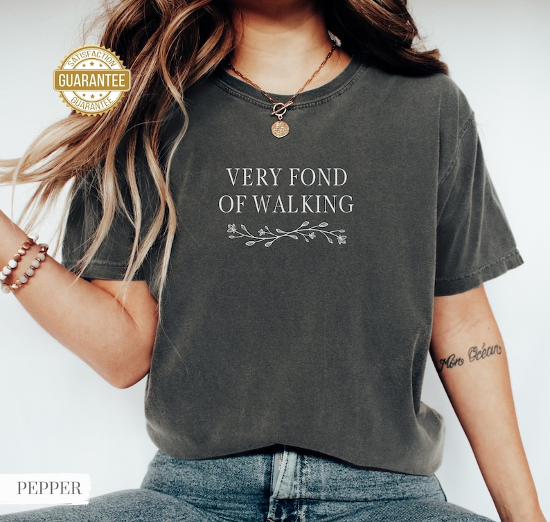 May include: Dark gray t-shirt with the text "VERY FOND OF WALKING" in white, along with a floral design. The shirt has a vintage, worn look. The word "PEPPER" is at the bottom of the image.