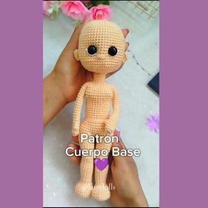 May include: A crocheted doll base with a nude color and black eyes. The doll is being held by a person's hands. The text "Patrón Cuerpo Base" is visible below the doll.