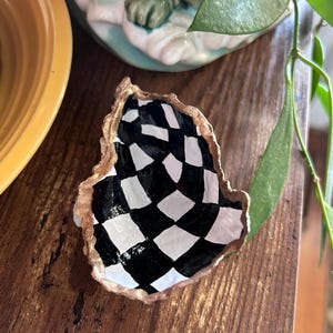 Può includere: Un motivo a scacchi bianco e nero dipinto su una conchiglia. La conchiglia è dorata e ha una texture ruvida.