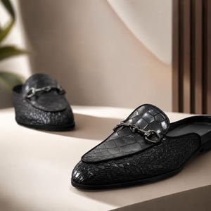 May include: A pair of black backless loafers featuring a textured crocodile-embossed leather finish and a pointed toe. Each shoe is adorned with a polished dark metal horsebit hardware detail across the vamp, creating a sleek and structured appearance.