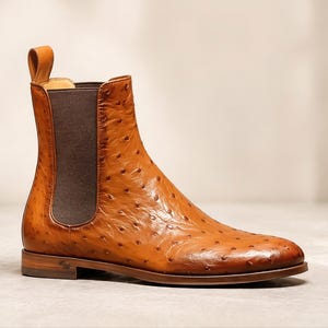 Peut inclure: Une botte Chelsea en cuir bronzé avec une languette et un panneau latéral élastique. La botte présente un motif texturé et pointillé et un petit talon. La botte mesure environ 25 cm de haut.