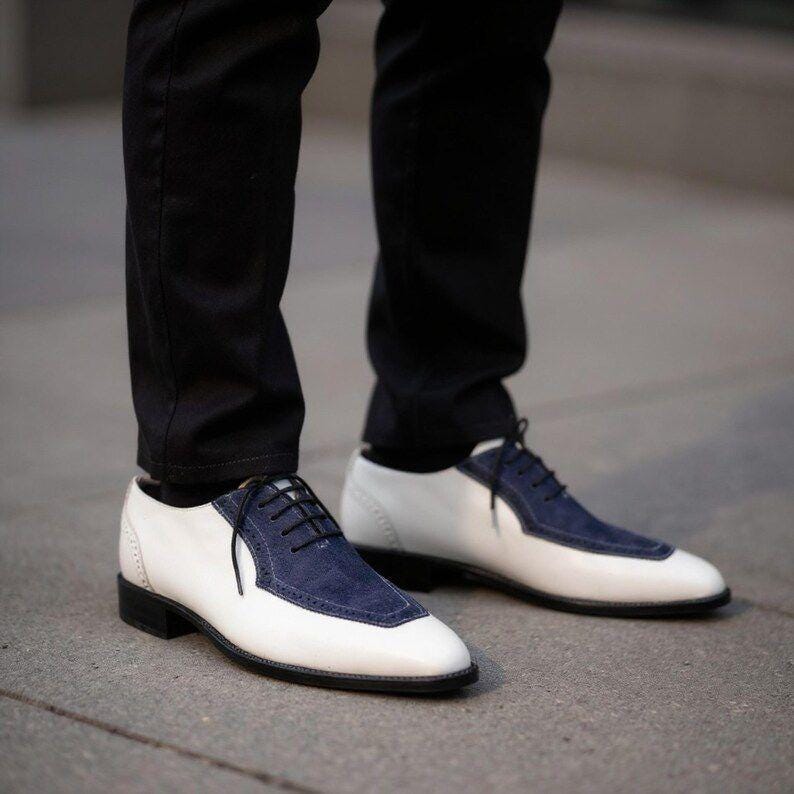 May include: Two-tone dress shoes featuring white leather and navy blue suede panels. The shoes have black laces and soles. A classic design suitable for formal events.