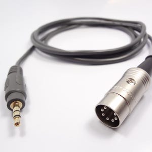 May include: A gray audio cable with a 3.5mm jack on one end and a silver XLR connector on the other. The cable is coiled and lies on a white surface. The XLR connector has multiple pin holes.