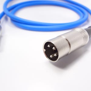 Pode incluir: Um cabo azul com dois conectores DIN prateados. Um conector tem 5 pinos e o outro tem 9 pinos.