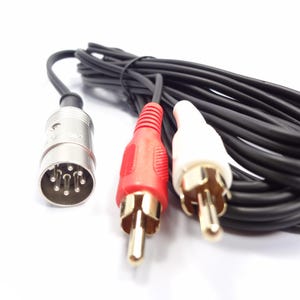 Puede incluir: Un cable de audio negro con un conector plateado y conectores RCA rojos y blancos. Los conectores RCA tienen puntas doradas. El cable está enrollado sobre una superficie blanca.