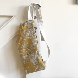 May include: A yellow fabric fanny pack with a white floral pattern and a gold zipper. The bag has a white canvas strap.