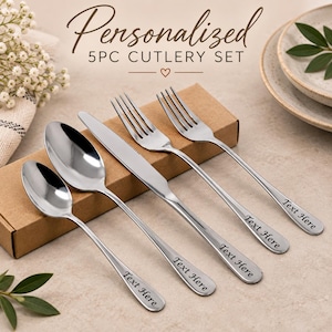 May include: A five-piece silver-toned stainless steel cutlery set including a small spoon, a large spoon, a knife, and two forks. Each handle features the engraved text "Text Here". The set is presented in a rectangular brown cardboard box.