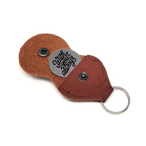 May include: A brown leather keychain case with a silver ring and a snap closure. Inside, a silver coin is visible, engraved with the words "With you always" in a script font. The case is open, revealing the coin.