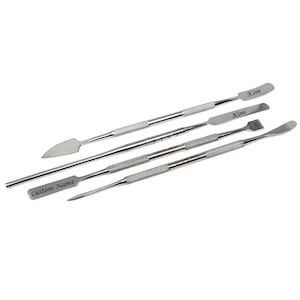 Peut inclure: Ensemble de cinq outils en métal argenté avec des manches texturés. Les outils ont des extrémités de formes différentes, dont une spatule et une pointe. Certains outils sont gravés des noms "Kim" et "Custom Name".