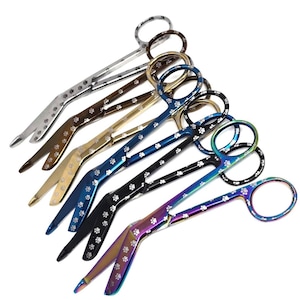 May include: A set of seven stainless steel bandage scissors with paw print designs. The scissors are in various colours, including silver, gold, brown, black, and rainbow.