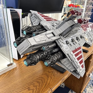 K&ouml;nnte beinhalten: Ein gro&szlig;es LEGO Star Wars Venator-Klasse Sternenzerst&ouml;rer-Modell aus grauen, wei&szlig;en und dunkelroten Kunststoffsteinen. Die R&uuml;ckansicht zeigt mehrere schwarze Triebwerke mit leuchtend hellblauen kreisf&ouml;rmigen Zentren und detaillierter H&uuml;lle.