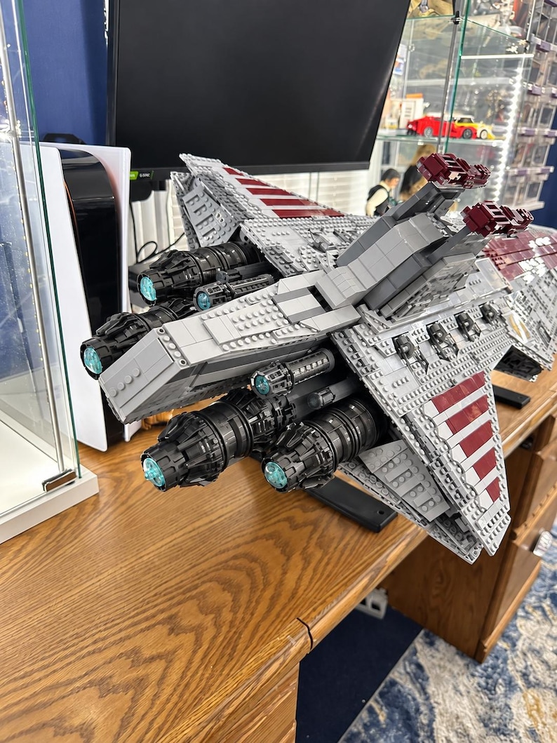 K&ouml;nnte beinhalten: Ein gro&szlig;es LEGO Star Wars Venator-Klasse Sternenzerst&ouml;rer-Modell aus grauen, wei&szlig;en und dunkelroten Kunststoffsteinen. Die R&uuml;ckansicht zeigt mehrere schwarze Triebwerke mit leuchtend hellblauen kreisf&ouml;rmigen Zentren und detaillierter H&uuml;lle.