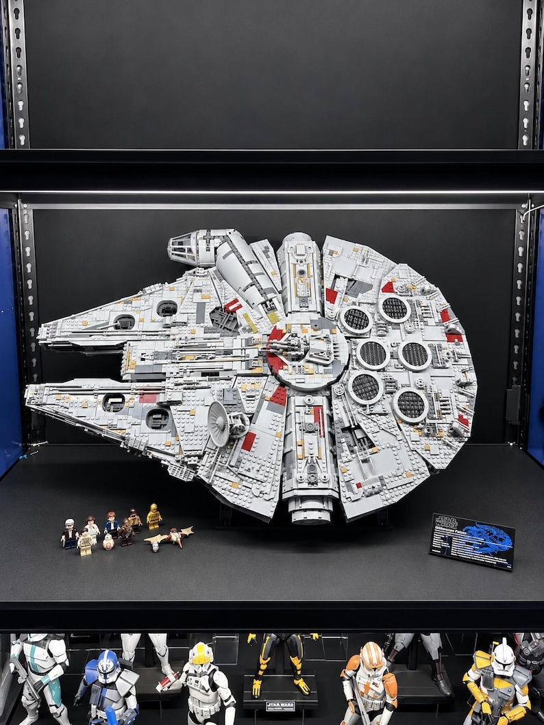 Pu&ograve; includere: Un grande e dettagliato modello LEGO Star Wars Millennium Falcon in grigio chiaro con accenti rossi, caratterizzato da uno scafo circolare, cabina di pilotaggio e parabola radar. Include diverse piccole minifigure e una targa informativa nera.