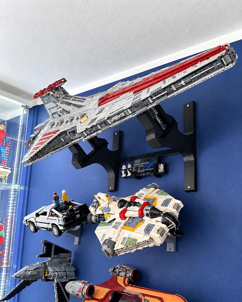 K&ouml;nnte beinhalten: Ein gro&szlig;es LEGO Star Wars Venator-class Republic Attack Cruiser Modell auf einer schwarzen Wandhalterung, positioniert &uuml;ber einem LEGO DeLorean, einem wei&szlig;-beigen Raumschiff, einem grauen Sternenj&auml;ger und einem orangefarbenen Raumschiff.