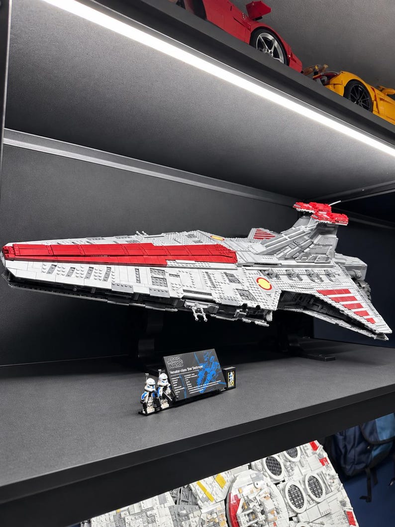 K&ouml;nnte beinhalten: Ein gro&szlig;es, detailliertes LEGO-Modell eines Venator-Klasse Sternenzerst&ouml;rers in Grau und Rot, montiert auf einem schwarzen St&auml;nder. Zwei kleine Klonkrieger-Minifiguren stehen neben einer schwarzen Infotafel mit wei&szlig;em Text zu den Schiffsdaten.